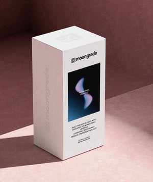 A white Moongrade product box standing upright on a pink surface against a mauve-pink background. The front of the box features a black square with a blue and pink abstract graphic and the Moongrade logo.