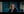 A blonde woman in a black top looks directly at the camera against a dark blue-toned blurred background. White text in the bottom right reads 'MG RED Log3G10 V2 Warm'.