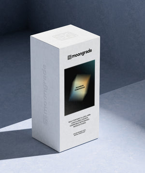 A white rectangular product box for moongrade, standing upright on a dark blue-gray surface against a matching dark background. The front of the box features a black square with a glowing yellow-green geometric shape and the text 'moonbow powergrade